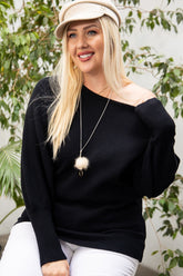 Plus size woman in black off-shoulder sweater, white pants, and beige hat with greenery background