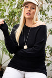 Plus size woman in black off-shoulder ribbed sweater, white pants, and beige hat, styled with pom-pom necklace