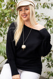 Plus size woman in black off-shoulder sweater, white pants, and beige hat with greenery background